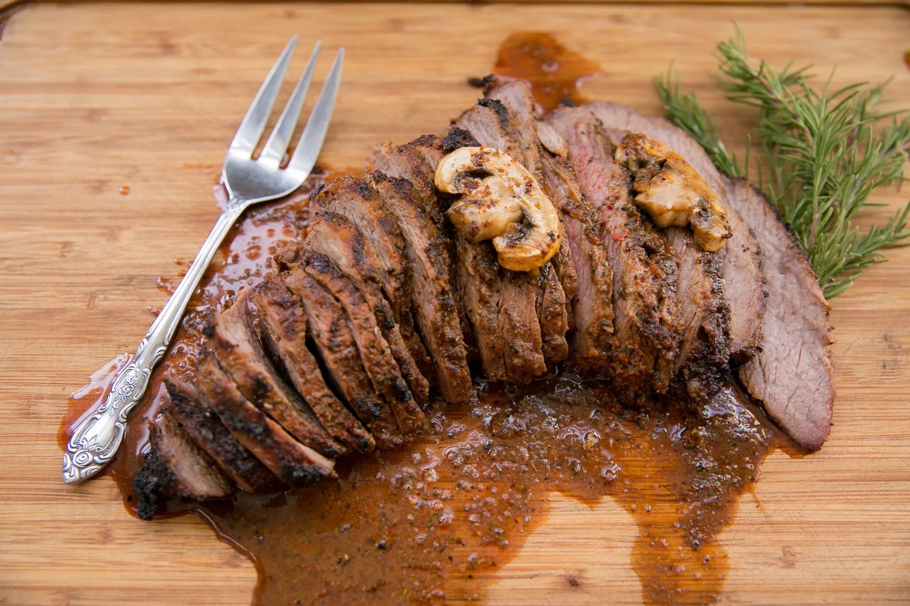 Sliced grilled steak with sautéed mushrooms on a cutting board